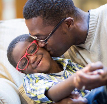 A man and a young girl in red glasses leaning close together and smiling.