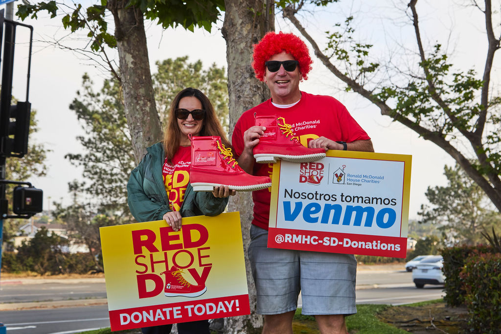 Tessa and Matt’s Red Shoe Crew volunteers hold Red Shoe Day donation signs and oversized red shoes at a San Diego intersection.