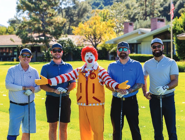 Ronald McDonald poses with a foursome of golfers on the course.
