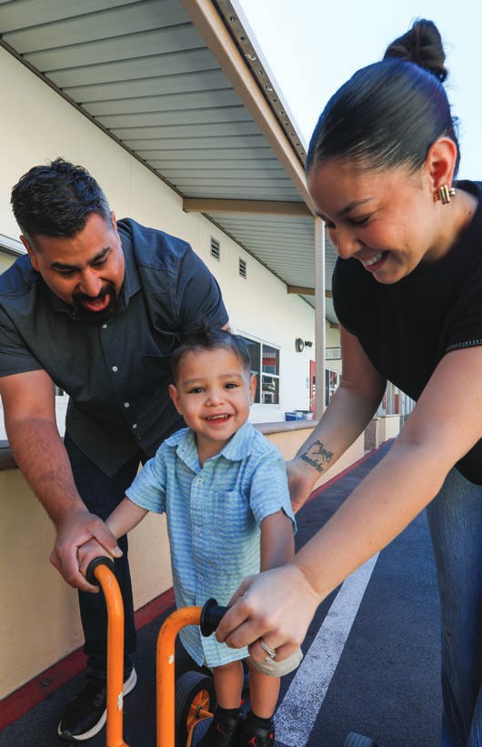 Jose and Alexandrea smile as they help their toddler son Jimmy stand at a play area at the House.