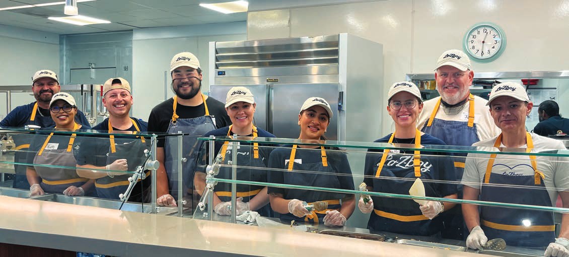 La-Z-Boy volunteers in aprons and caps smile behind the serving line in the House kitchen.