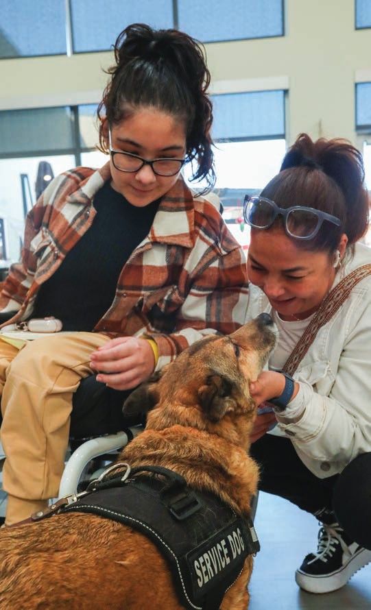 Two young women smile as they pet a visiting therapy dog.
