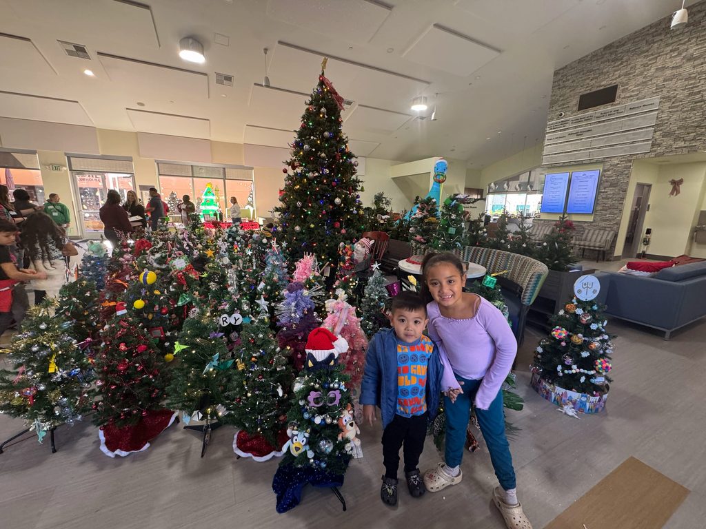Amelia and Clyde Camara smile in front of the mini Christmas trees in the great room at Ronald McDonald House San Diego